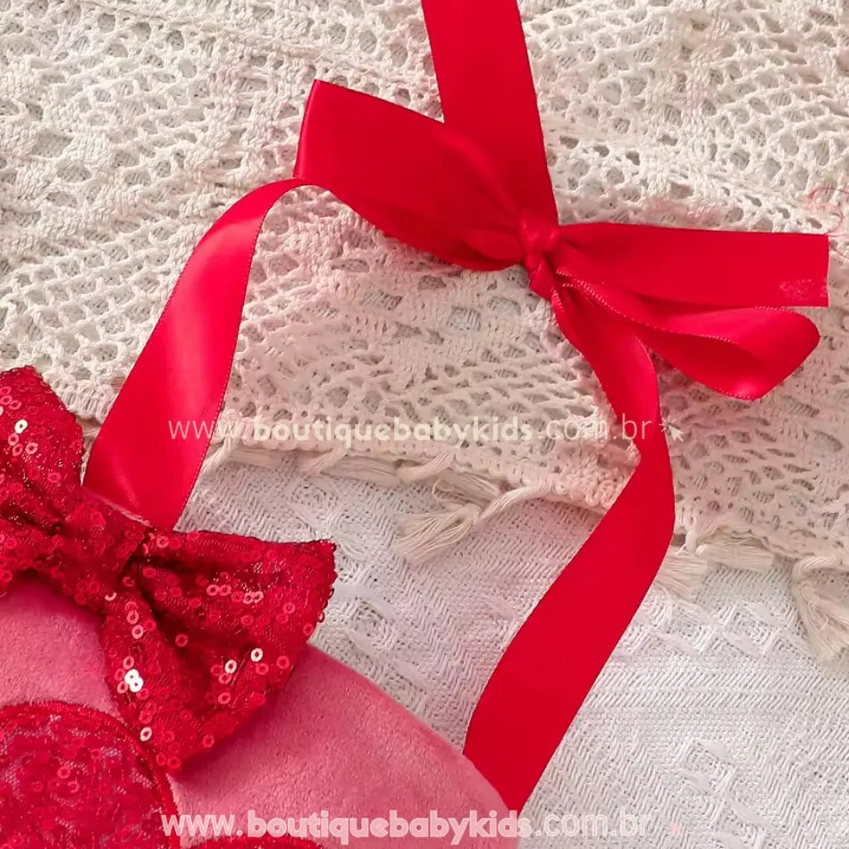 Laço de fita vermelha para amarração nos ombros, permitindo ajuste perfeito e um acabamento delicado. Fundo com renda branca e decoração temática romântica.