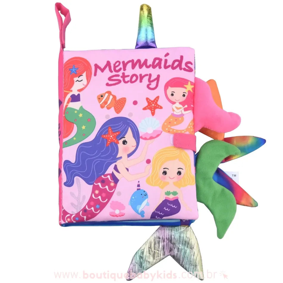 Capa do Livro Sensorial para Bebê Mundo das Sereias 3D, com fundo rosa e ilustrações coloridas de sereias, conchas e estrelas-do-mar. As laterais do livro possuem caudas de sereia em tecido macio, destacando-se para a interação sensorial.