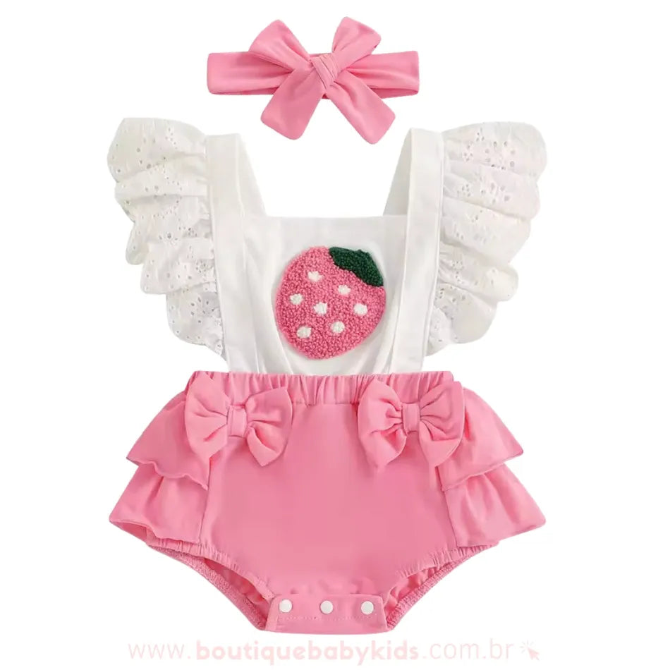 Romper bebê cor-de-rosa com bordado de morango no peitinho, alças com babados rendados brancos e parte inferior com babados e laços decorativos. Acompanha uma faixa de cabelo rosa com laço.