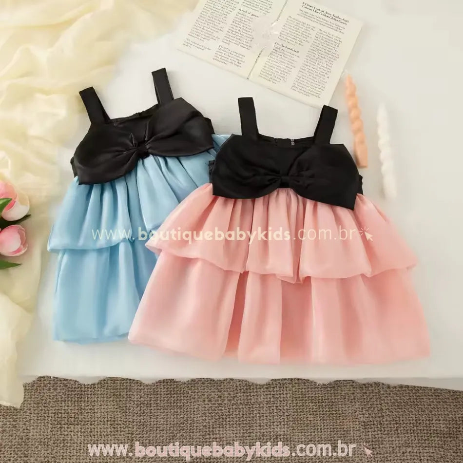 Vestidos infantis azul e rosa com busto preto e saia em camadas de tule, dispostos lado a lado.