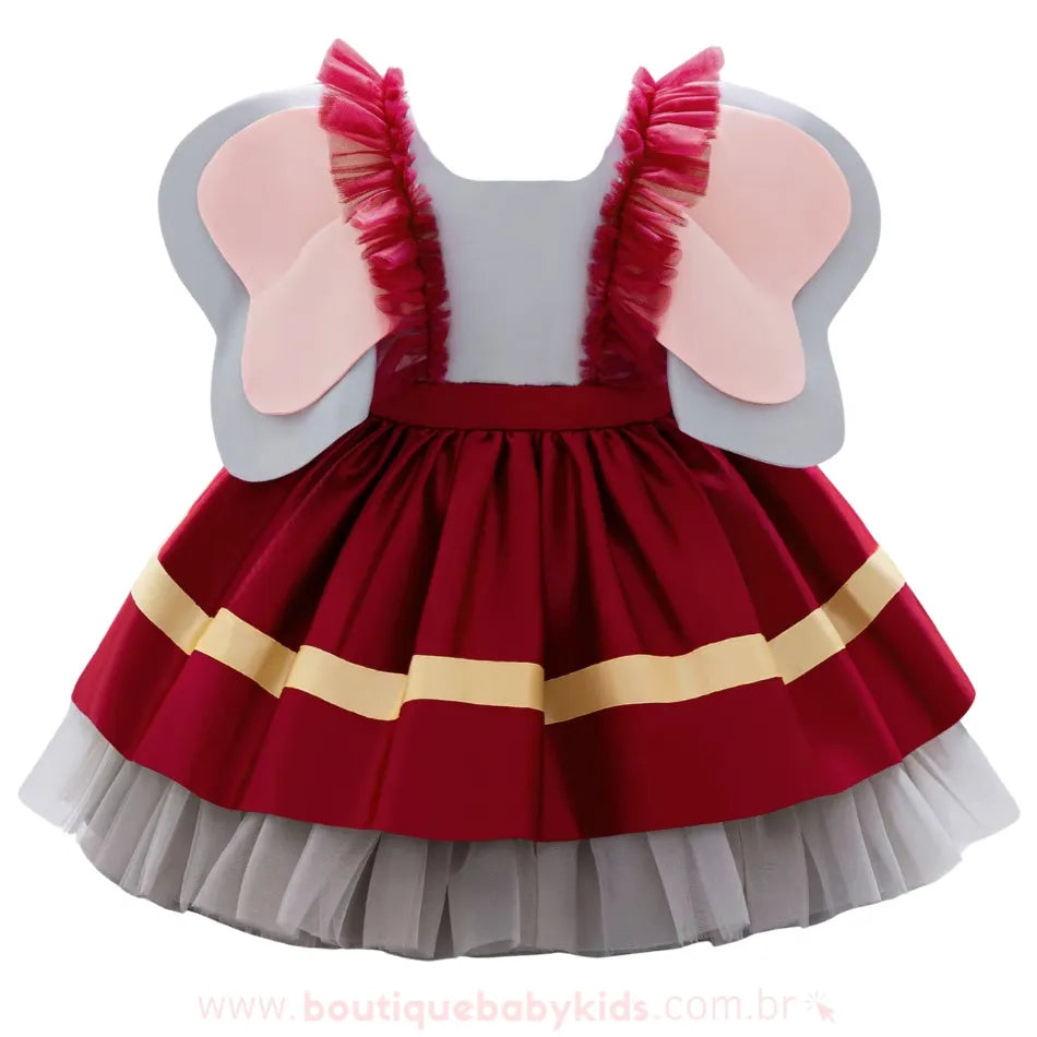 Vestido inspirado no elefante Dumbo visto de costas, com saia vermelha de detalhes dourados, camadas de tule cinza e grandes orelhas fixas nas alças de babado em tule vermelho.