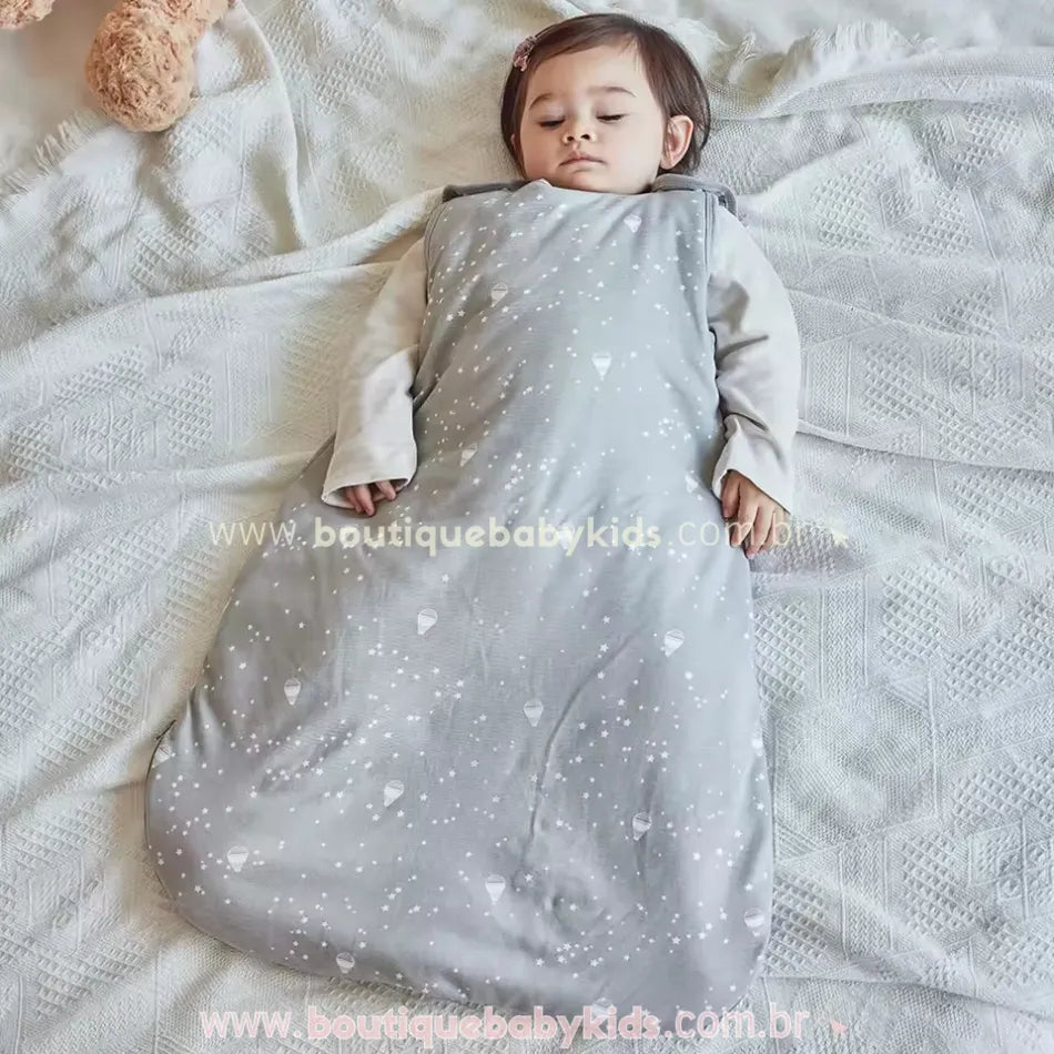 Bebê dormindo confortavelmente dentro do saco de dormir cinza, que cobre todo o corpinho, deixando apenas a cabeça e os braços livres.