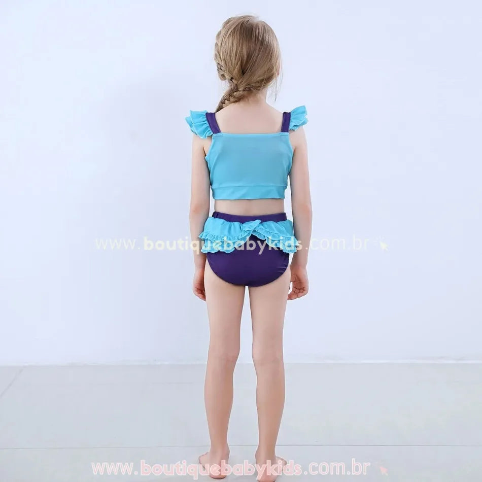 Vista traseira do Biquíni Infantil Princesa Ariel, mostrando o top azul-claro com alças finas e babados nos ombros, além da calcinha lilás com sobreposição de babados azul-claros na parte de trás, criando um efeito encantador.
