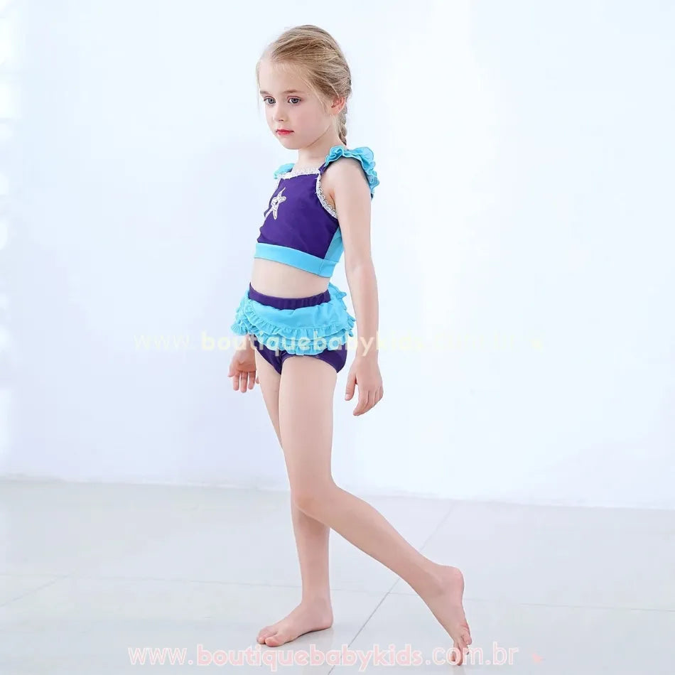 Menina posando de perfil com o Biquíni Infantil Princesa Ariel, destacando o caimento confortável e os detalhes delicados de renda e babados.