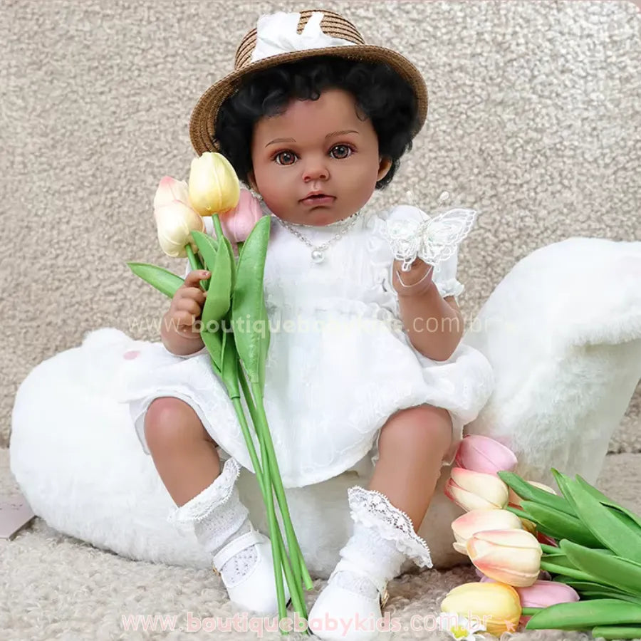 Boneca Bebê Reborn Cecília negra realista, vestindo vestido branco delicado e chapéu de palha, segurando tulipas coloridas em cenário suave.