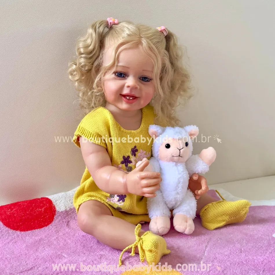 Boneca Lara sorrindo enquanto segura um ursinho de pelúcia branco e está sentada sobre toalha rosa.