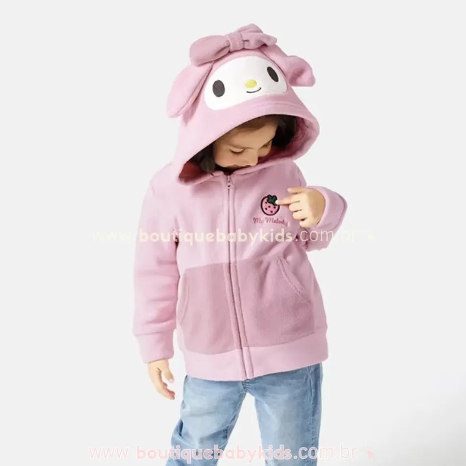 Menina usando a jaqueta My Melody com capuz colocado, apontando para o bordado – imagem lúdica que mostra a personagem no capuz.