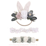 Kit de faixas para bebê com detalhes florais, incluindo uma faixa com orelhinhas de coelho de renda e flores cinza e brancas, uma faixa rendada delicada e uma faixa com pequenas rosas em tons neutros.