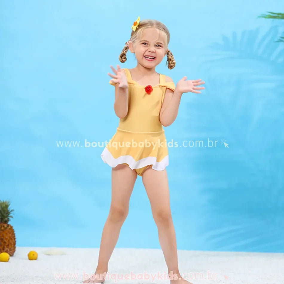 Menina loira sorrindo e brincando enquanto veste o maiô infantil Princesa Bela, mostrando a leveza e fluidez do modelo, com um fundo azul claro.