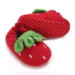 Close das pantufinhas vermelhas de morango nos pés do bebê, destacando a sola antiderrapante. 