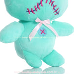 Detalhe do laço branco de cetim e botão bordado azul na barriga da pelúcia Scrump, com costura decorativa em rosa.