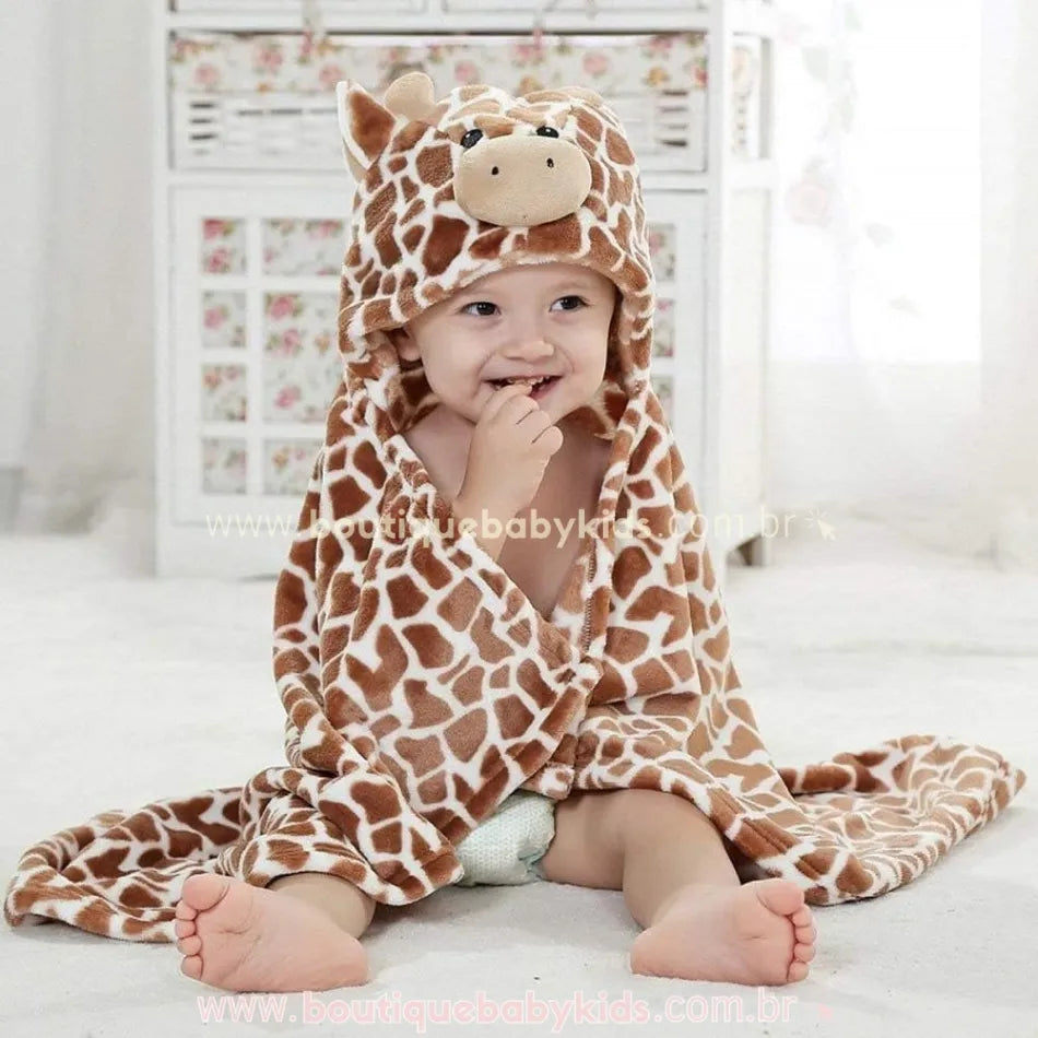 Bebê sorrindo enquanto usa a toalha com capuz de girafinha, transmitindo um momento de conforto e diversão após o banho.