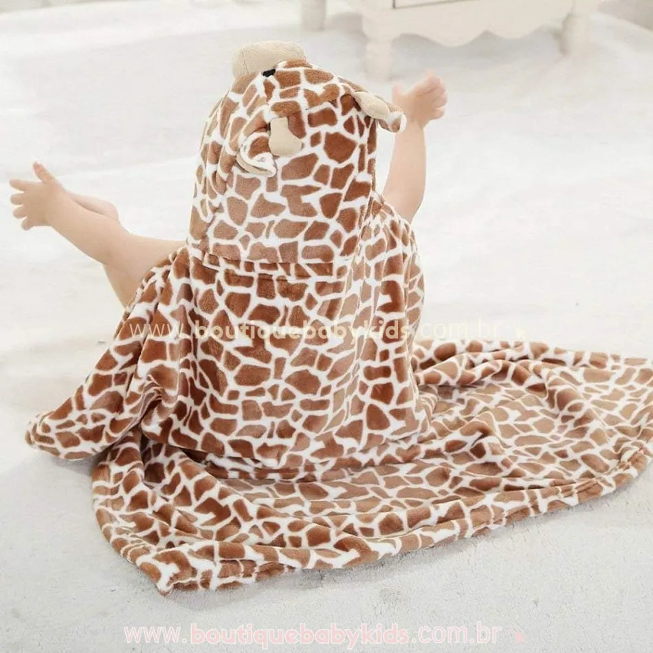 Bebê sentado no chão usando a Toalha Bebê Divertida Girafinha, com capuz temático que imita o rostinho de uma girafa, cobrindo parte do corpo e criando um visual aconchegante.